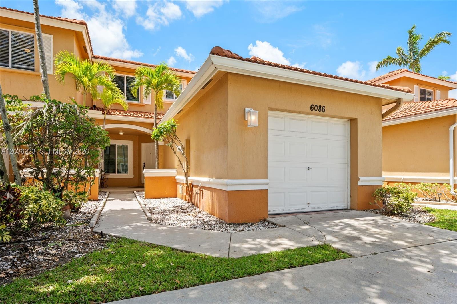 A two-story tan stucco townhouse features a single-car garage and a paved walkway — 6086 Southard St, West Palm Beach FL 33411, WEST PALM BEACH, FL