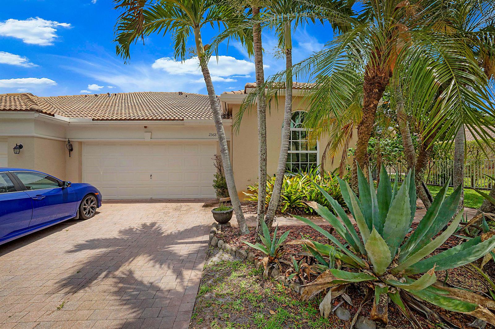 A blue car is parked on a paved driveway in front of a tan house — 2568 Sandy Cay, West Palm Beach FL 33411, WEST PALM BEACH, FL