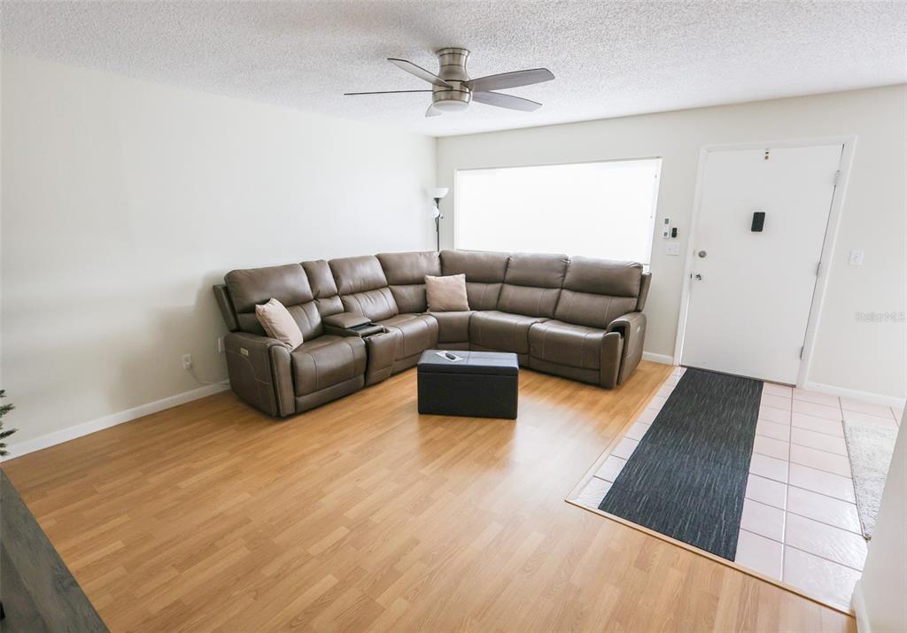 A living room features a large brown sectional sofa, wood-look flooring, and a ceiling fan — 1235 S HIGHLAND AVENUE UNIT 4-306, CLEARWATER, FL