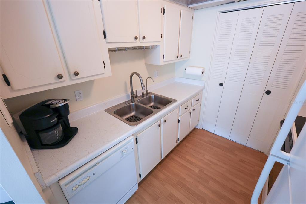 A kitchen features white cabinets, a double-basin sink, a dishwasher, and light wood-look flooring — 1235 S HIGHLAND AVENUE UNIT 4-306, CLEARWATER, FL