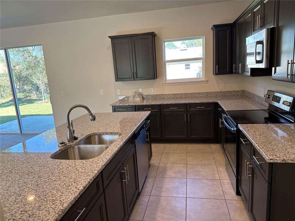 A kitchen features dark wood cabinets, granite countertops, a center island, and tile flooring — 1464 SHADOW LANE, NORTH PORT, FL