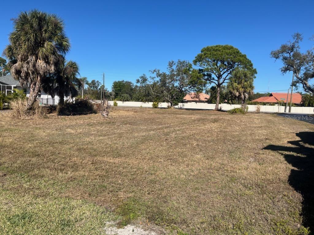 A flat, grassy vacant lot features scattered trees and a white fence in the background — 0 LAUREL WOODS DRIVE, NOKOMIS, FL