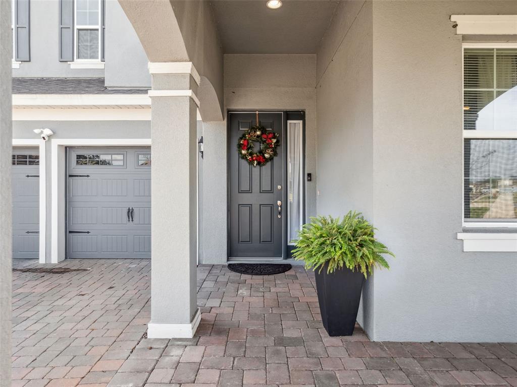 A gray house exterior features a paved walkway, a dark front door with a wreath, and a potted plant — 591 VIA BELLA COURT, HOWEY IN THE HILLS, FL
