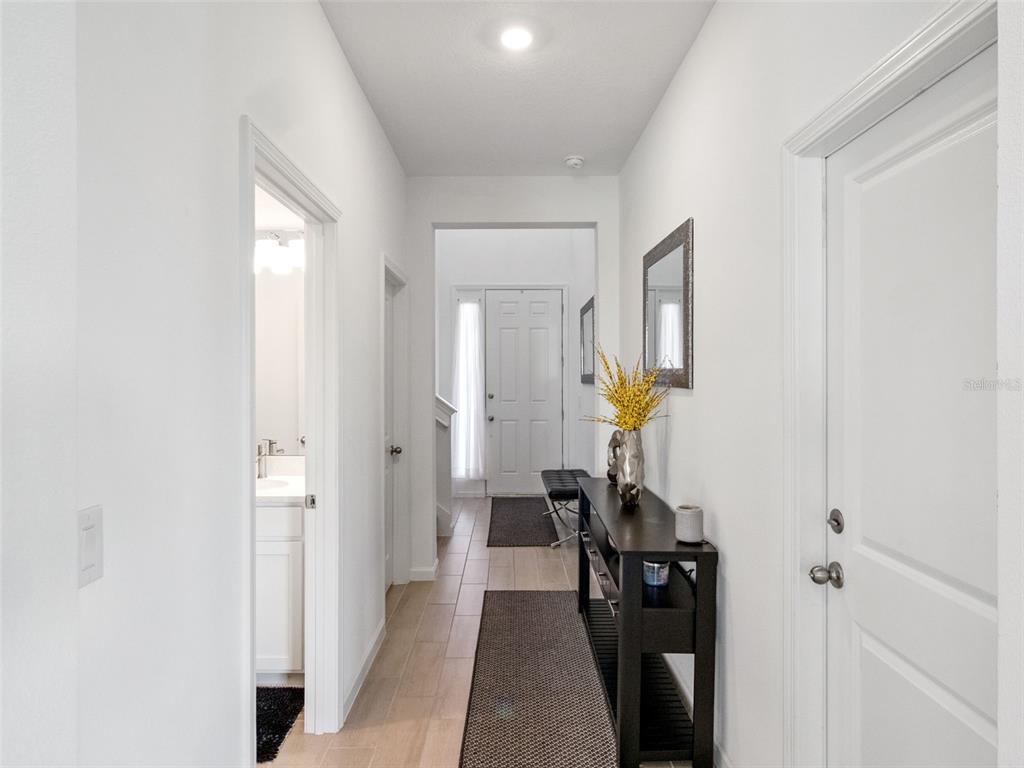 A hallway with light tile flooring leads to a front door with a console table — 591 VIA BELLA COURT, HOWEY IN THE HILLS, FL
