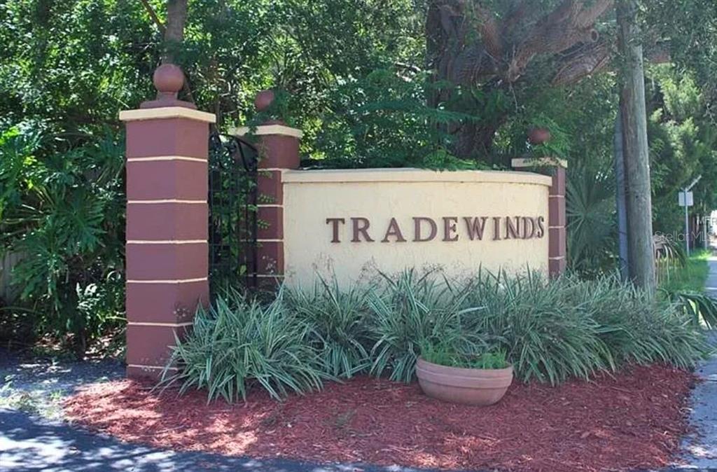 A curved beige monument sign with the word Tradewinds stands in a landscaped garden area — 353 S MCMULLEN BOOTH ROAD UNIT 133, CLEARWATER, FL