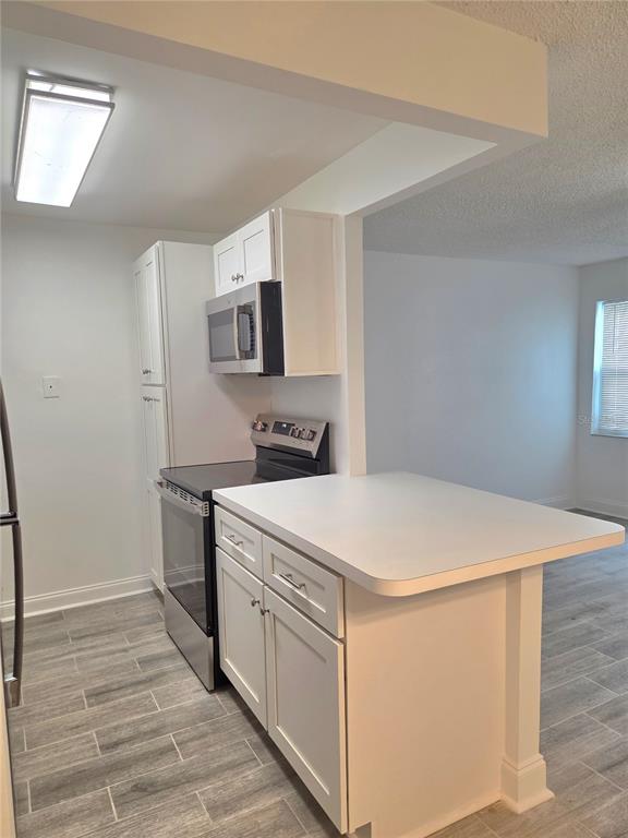A kitchen with white cabinets, stainless steel appliances, and gray wood-look tile flooring — 353 S MCMULLEN BOOTH ROAD UNIT 133, CLEARWATER, FL