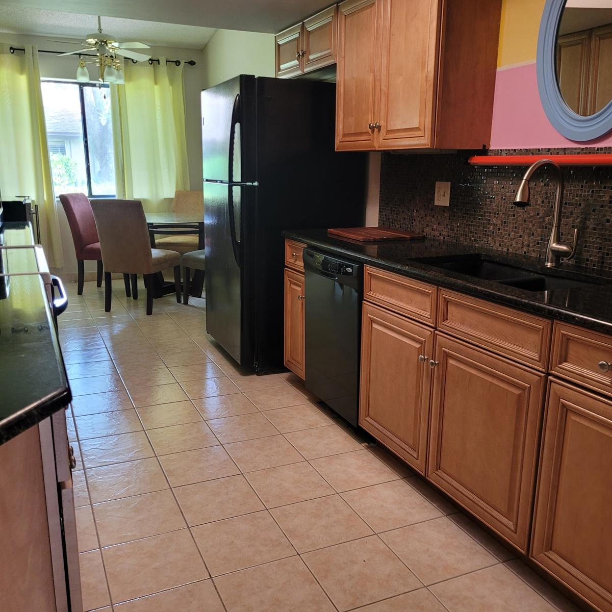 A kitchen with wood cabinets, black appliances, dark countertops, and tile flooring — 135 Meander Circle, Royal Palm Beach FL 33411, ROYAL PALM BEACH, FL