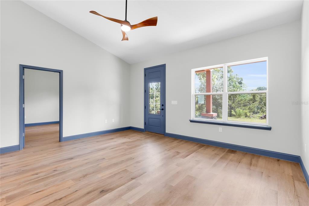 An empty room with light wood floors, blue trim, a ceiling fan, and a glass door — 1170 CR 543B, SUMTERVILLE, FL