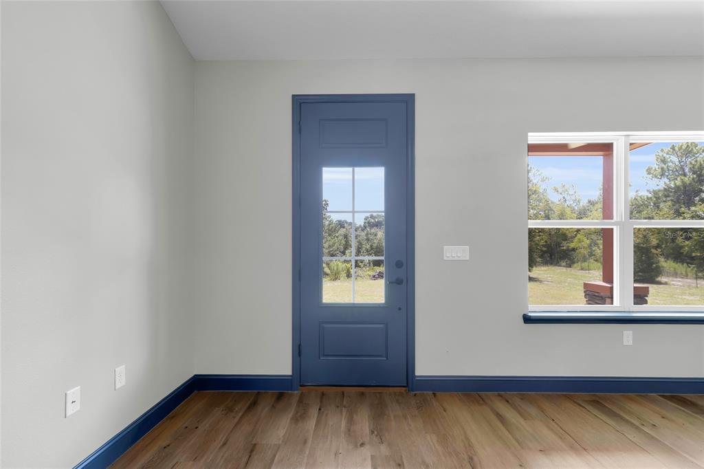 A room with light gray walls, wood-look flooring, a blue door, and a large window — 1170 CR 543B, SUMTERVILLE, FL