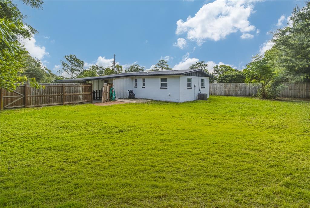 A white one-story house with a metal roof sits in a large, grassy backyard — 465 SIGSBEE COURT, ORANGE PARK, FL