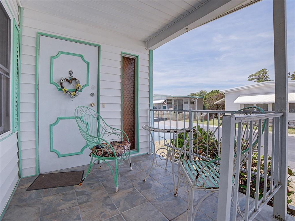 A covered porch with tiled flooring, metal furniture, and a white door with mint trim — 701 SUGAR PALM STREET, LARGO, FL