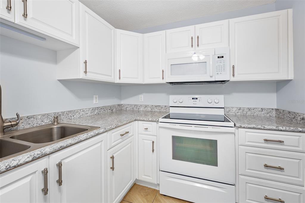 A kitchen with white cabinets, granite countertops, and white appliances — 2711 N HALIFAX AVENUE UNIT 478, DAYTONA BEACH, FL