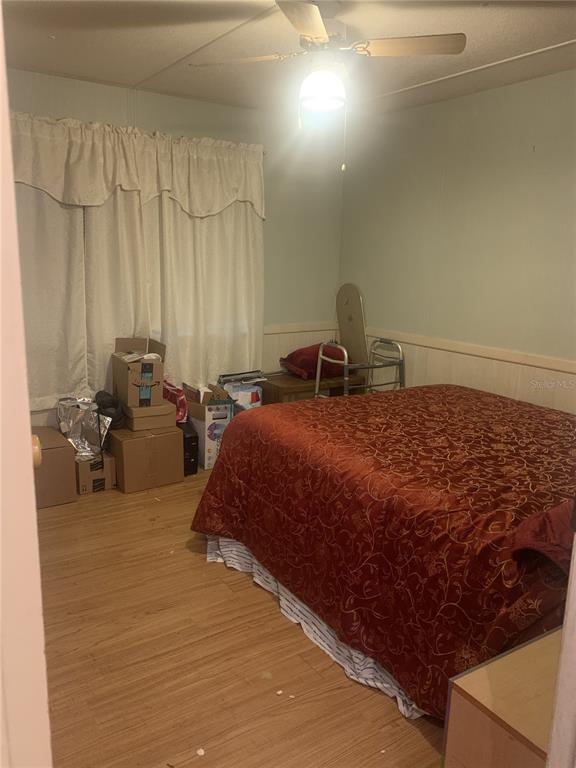 A bedroom with light wood-look flooring, a red patterned bedspread, and boxes near the window — 14391 SANDHURST STREET, BROOKSVILLE, FL