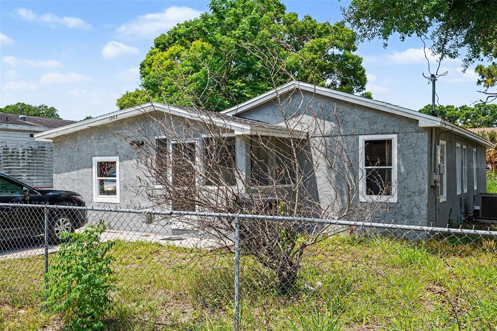 A single-story gray house with a screened porch is viewed behind a chain-link fence — 1303 37TH STREET NW, WINTER HAVEN, FL