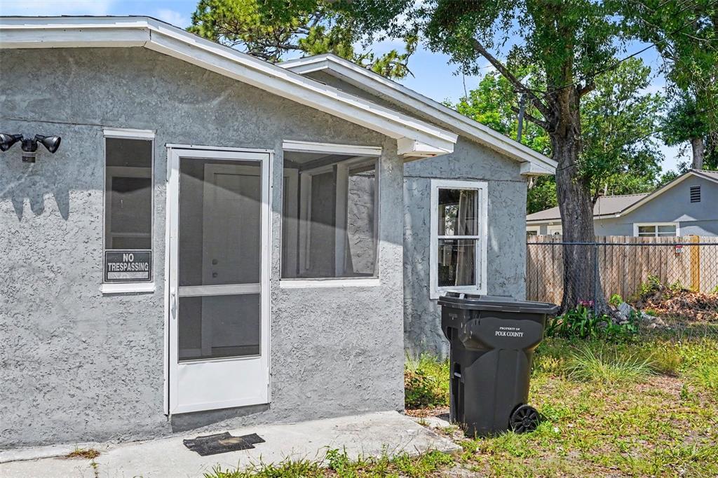 A gray stucco exterior wall features a screen door, two windows, and a trash bin — 1303 37TH STREET NW, WINTER HAVEN, FL