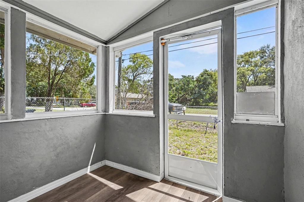 A sunroom features gray walls, wood-look flooring, large windows, and a white screen door — 1303 37TH STREET NW, WINTER HAVEN, FL