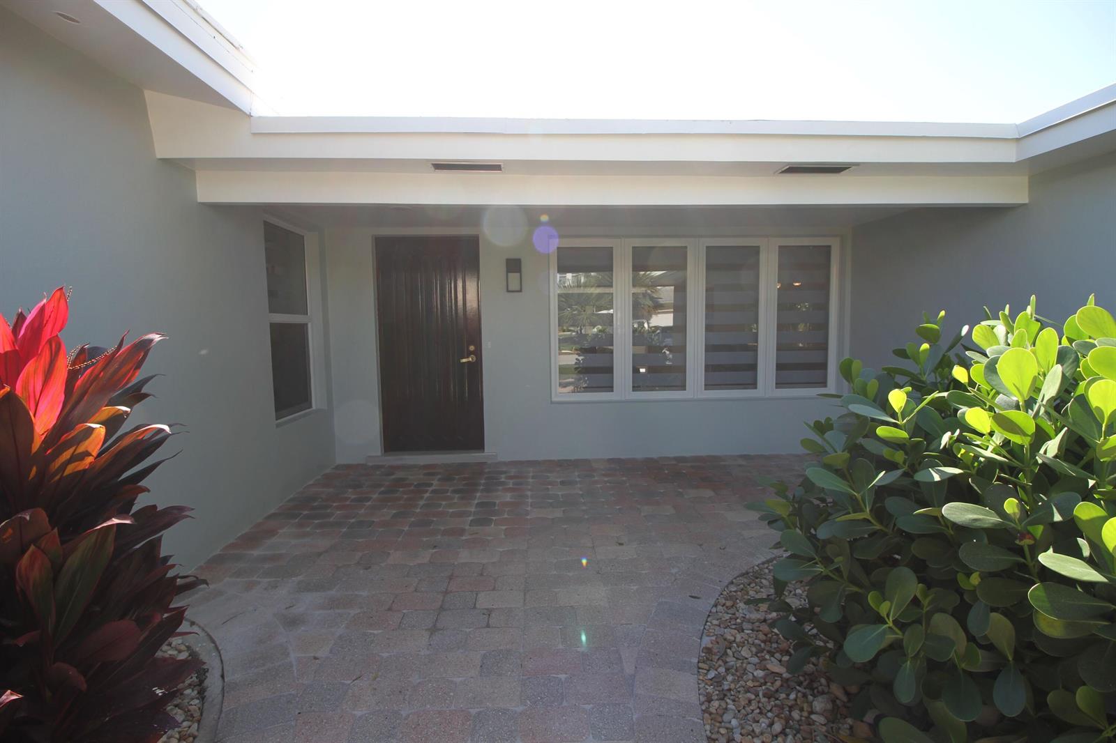 A covered entryway features a dark wood front door, large windows, and a paved patio — 2548 SE 14th Street E, Pompano Beach FL 33062, POMPANO BEACH, FL