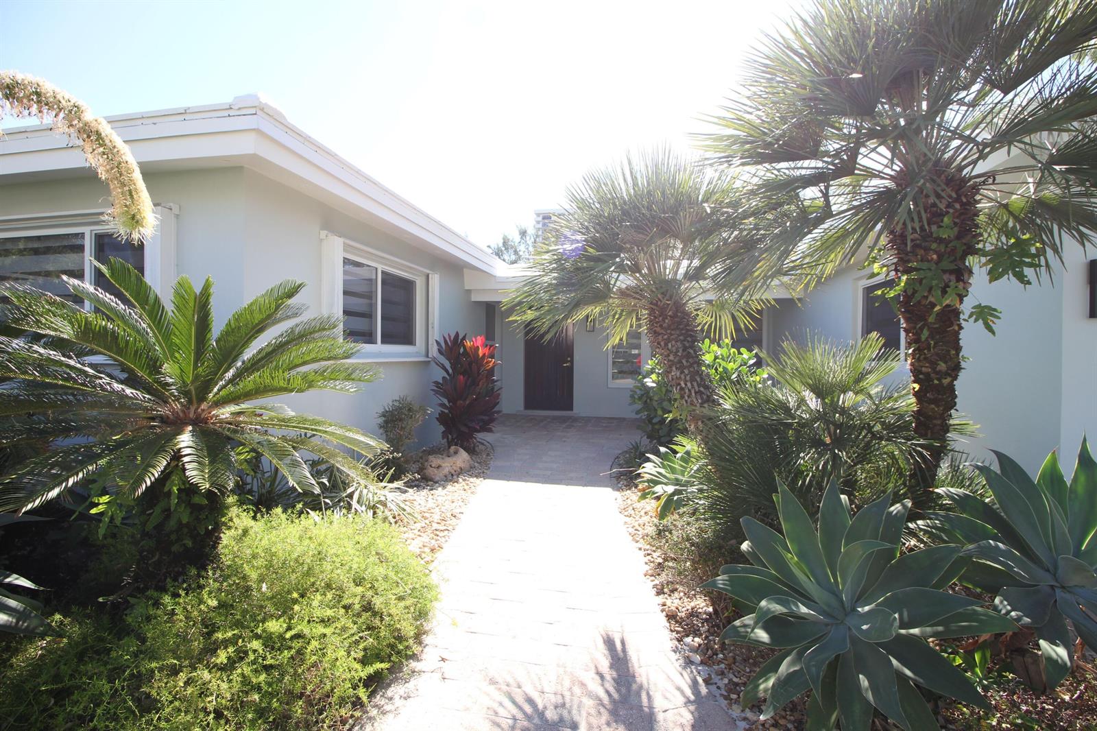 A paved walkway leads to the front entrance of a house surrounded by tropical landscaping — 2548 SE 14th Street E, Pompano Beach FL 33062, POMPANO BEACH, FL