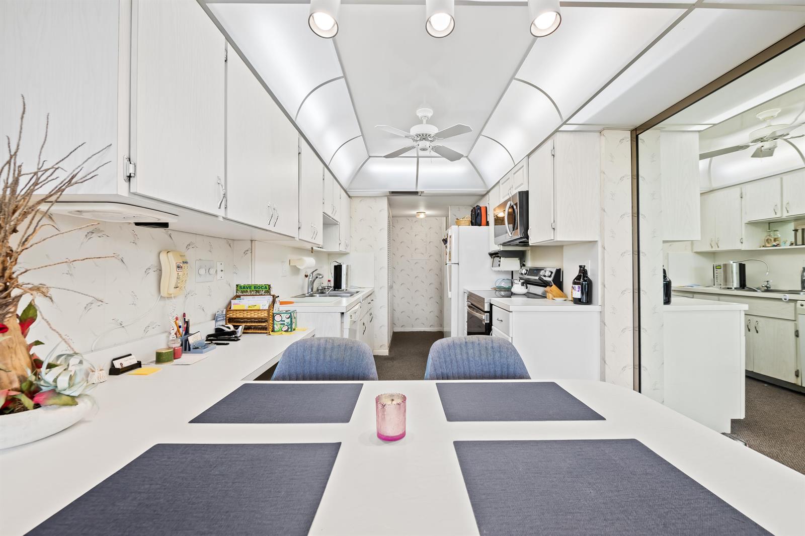 A galley kitchen features white cabinetry, a dining table with blue placemats, and recessed lighting — 799 Jeffery Street # 4050, Boca Raton FL 33487, BOCA RATON, FL