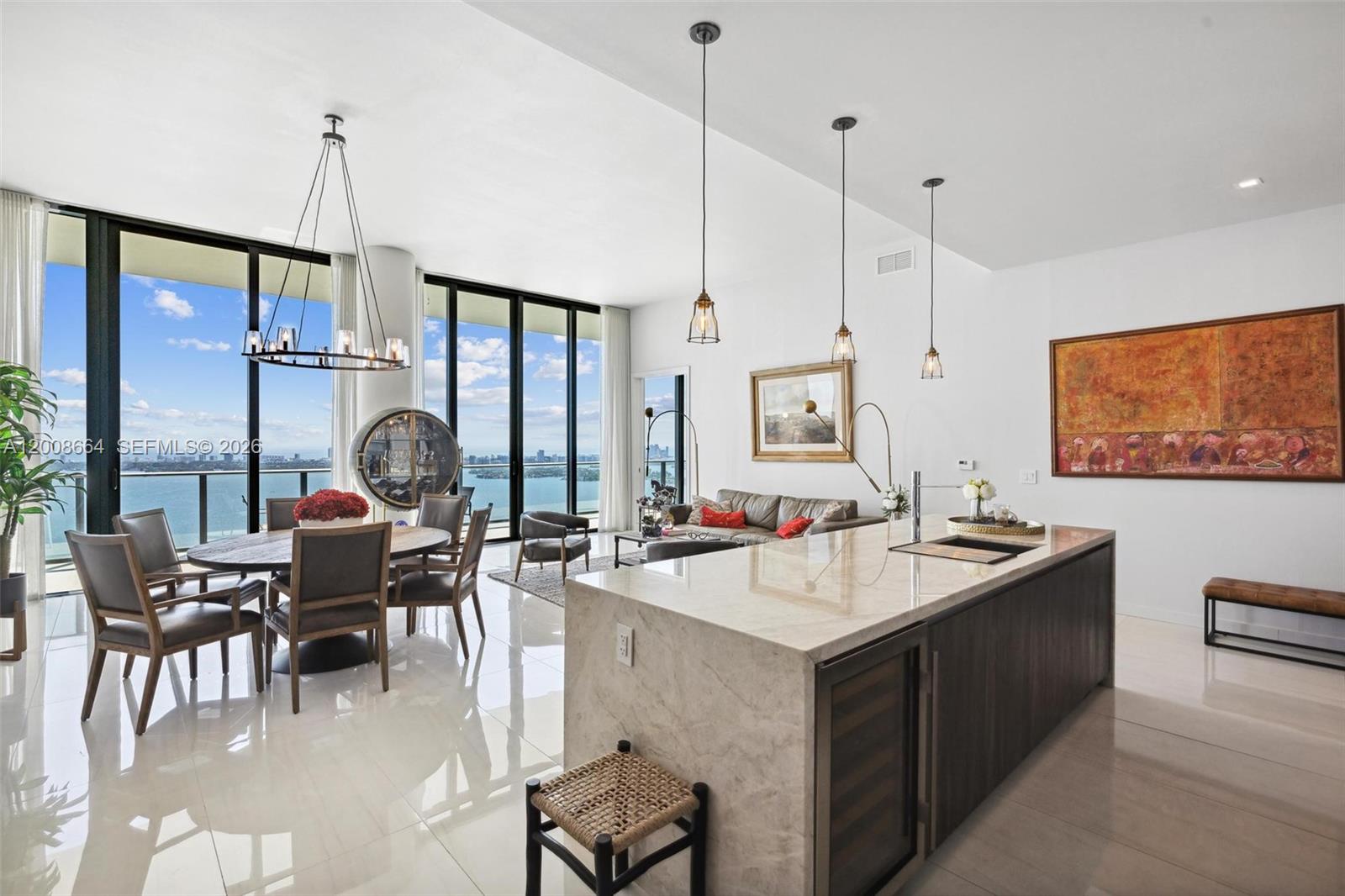 A modern open-concept living and dining area features a marble island, floor-to-ceiling windows, and water views — 480 NE 31st St, Miami FL 33137, MIAMI, FL