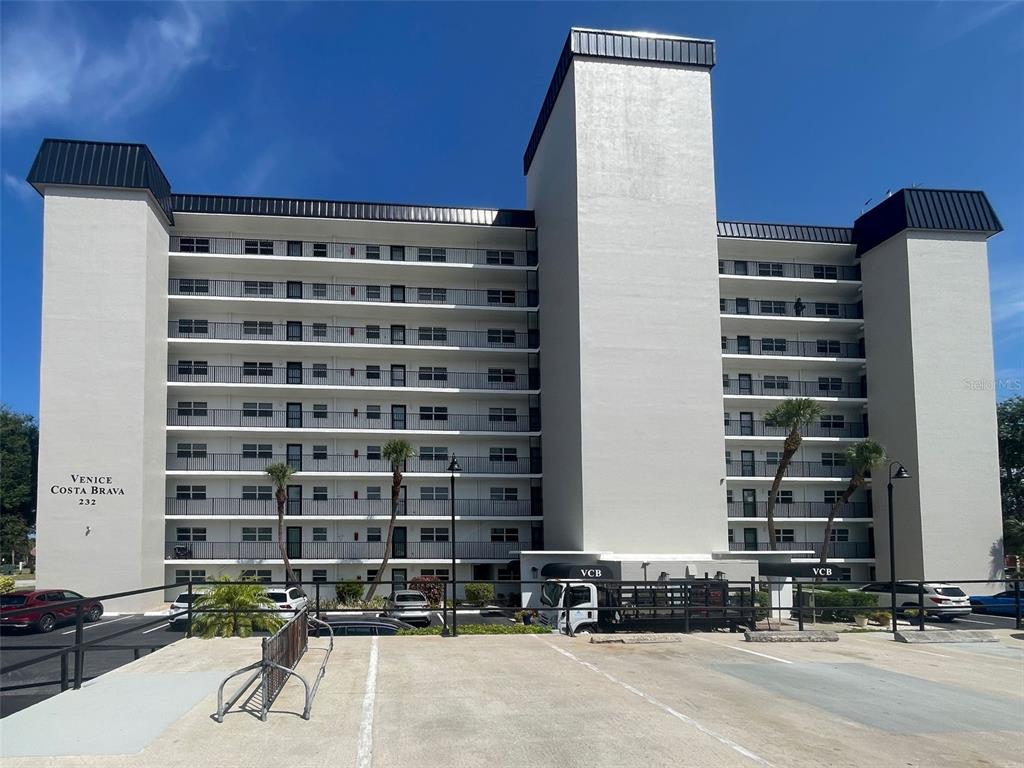 A multi-story apartment building with balconies and a parking lot in the foreground — 232 SAINT AUGUSTINE AVENUE UNIT 207, VENICE, FL