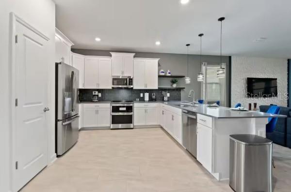 A modern kitchen features white cabinetry, stainless steel appliances, and a large island with seating — 9254 SOMMERSET HILLS DRIVE, DAVENPORT, FL