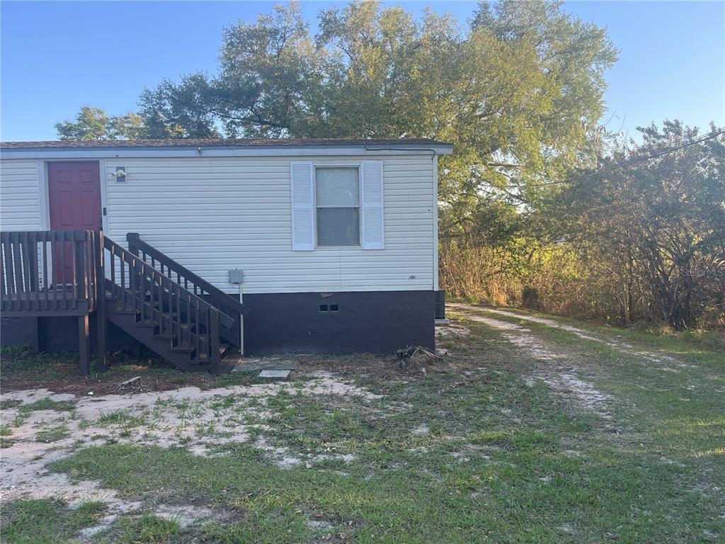 The exterior of a light-colored mobile home features a dark-painted foundation and wooden stairs — 142 WINSTON AVENUE, LAKE WALES, FL