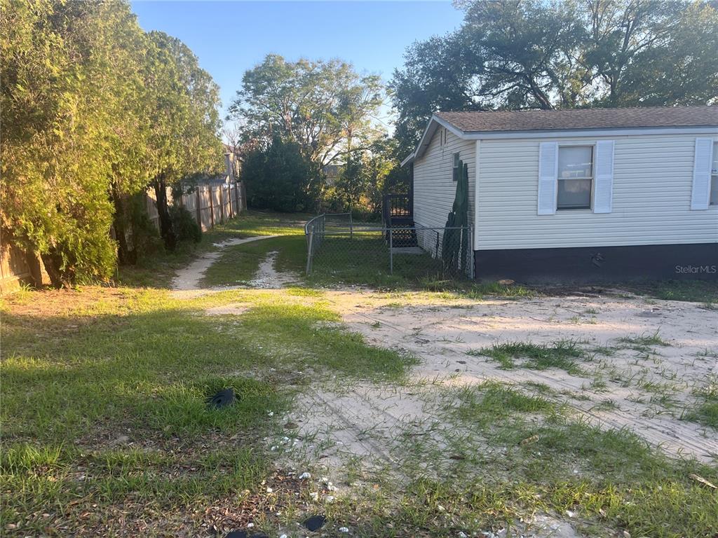 A side view of a light-colored mobile home with a small fenced yard and driveway — 142 WINSTON AVENUE, LAKE WALES, FL
