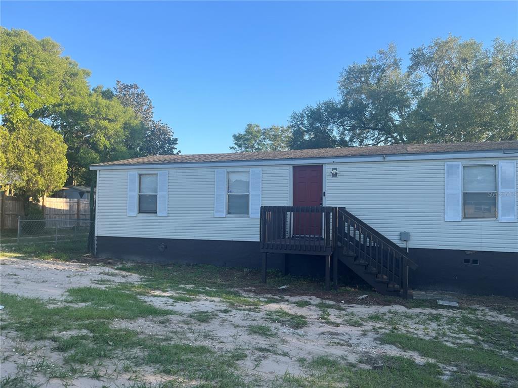 A single-story manufactured home with light siding, a red front door, and a wooden deck — 142 WINSTON AVENUE, LAKE WALES, FL