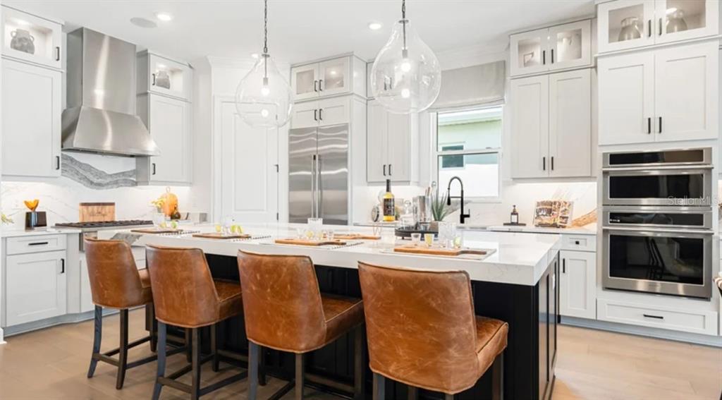 A modern kitchen features white cabinetry, a large black island with leather stools, and stainless appliances — 7391 MOONBEAM AVENUE, SARASOTA, FL