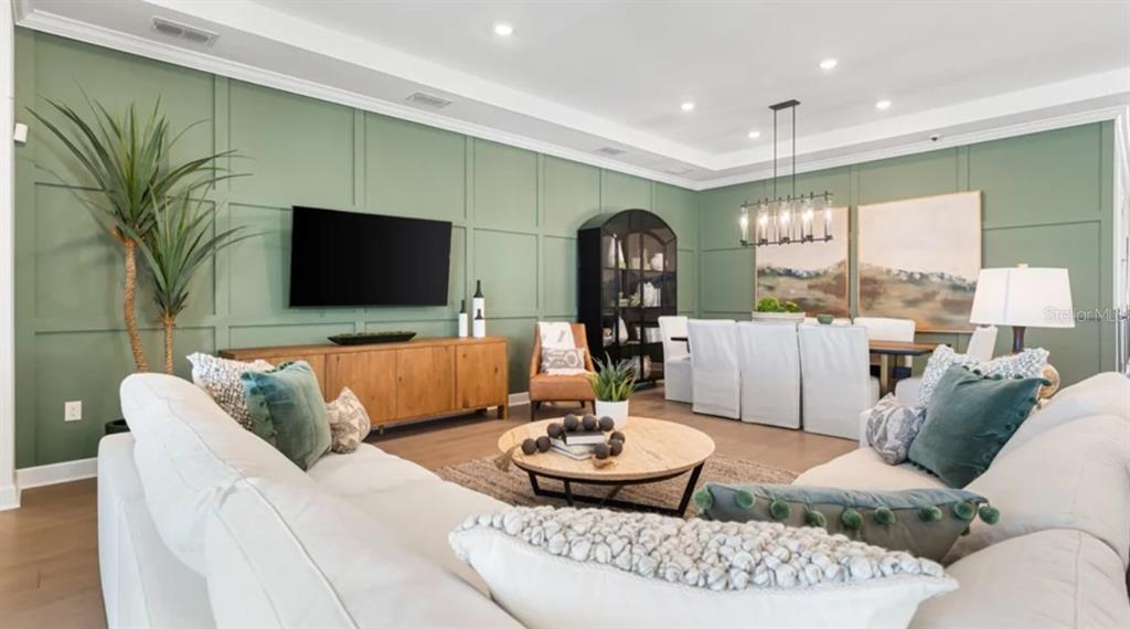 A living and dining room with sage green paneled walls, white sofas, and wood furniture — 7391 MOONBEAM AVENUE, SARASOTA, FL