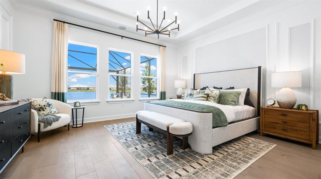 A bedroom features a king bed, a sitting area, and large windows overlooking a lake — 7391 MOONBEAM AVENUE, SARASOTA, FL