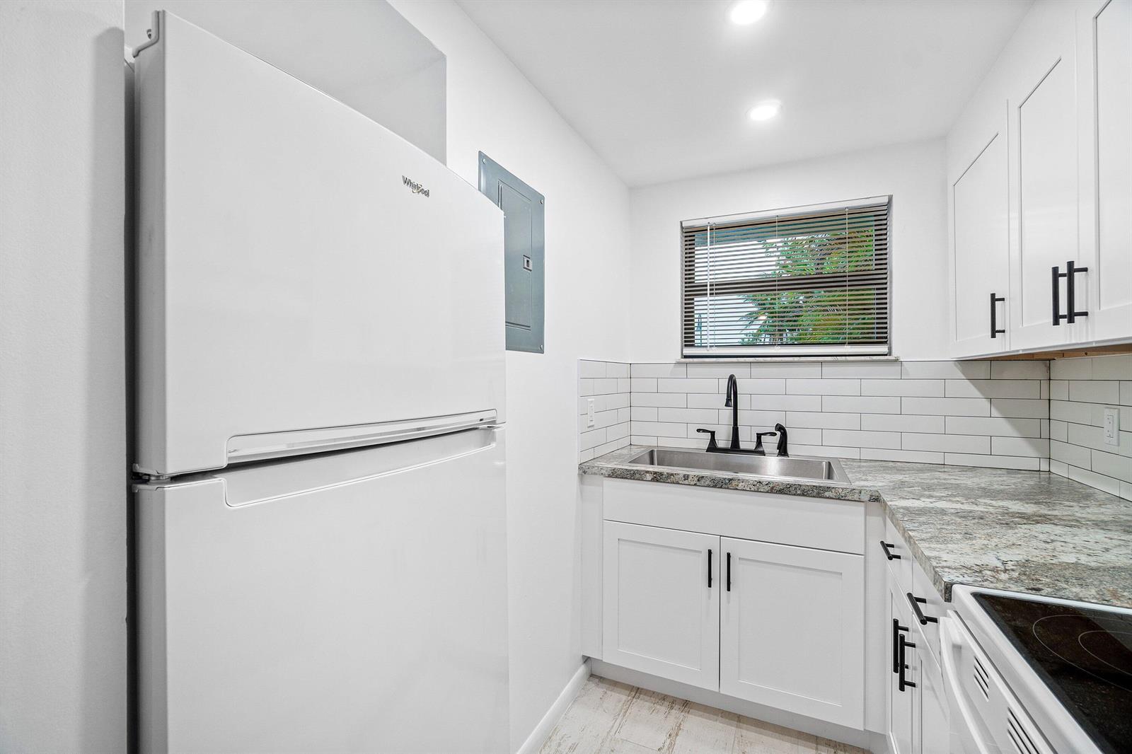 A white kitchen features a Whirlpool refrigerator, subway tile backsplash, and dark cabinet hardware — 626 N Federal Highway Unit 3, FL 33460, FL