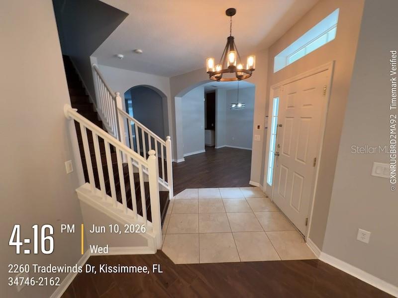 An entryway features tile flooring, a dark wood staircase with white railings, and a chandelier — 2260 TRADEWINDS DRIVE, KISSIMMEE, FL