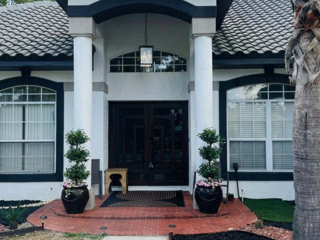 The front entrance features a double door, two white columns, and potted topiary trees — 1043 W SEAGATE DRIVE, DELTONA, FL