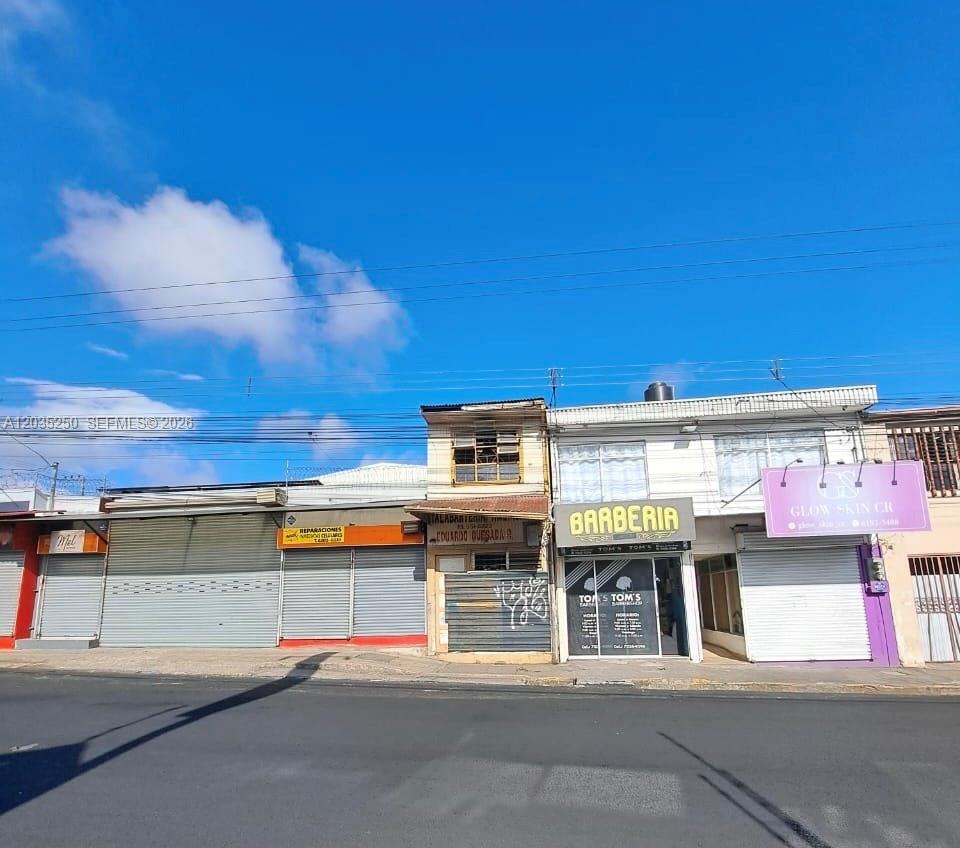 A row of commercial storefronts with metal roll-down doors and signage under a blue sky — Avenida Central Cartago, FL 000, FL