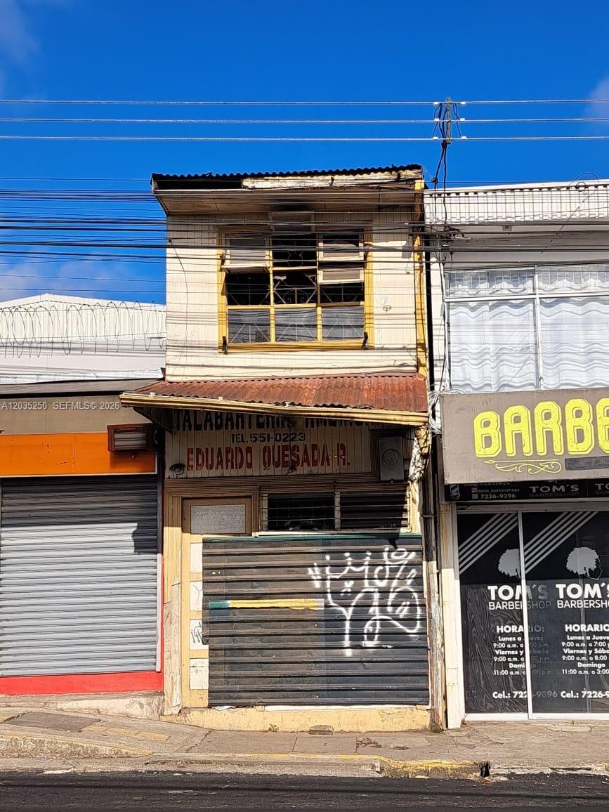 A narrow, two-story building with a weathered wooden facade sits between two commercial storefronts — Avenida Central Cartago, FL 000, FL
