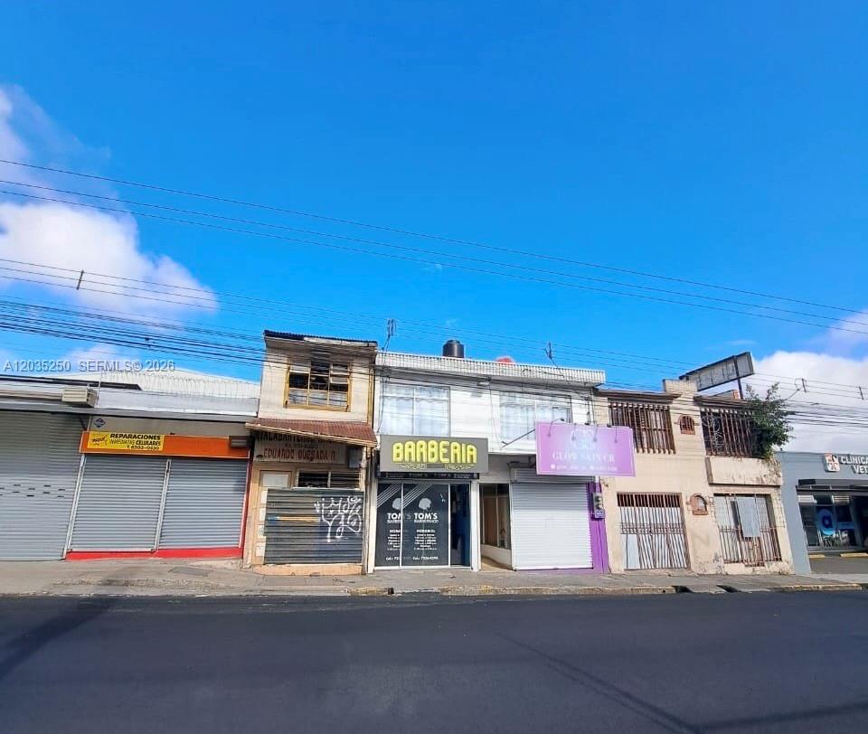 A row of commercial storefronts with metal shutters and signage along a street under blue sky — Avenida Central Cartago, FL 000, FL