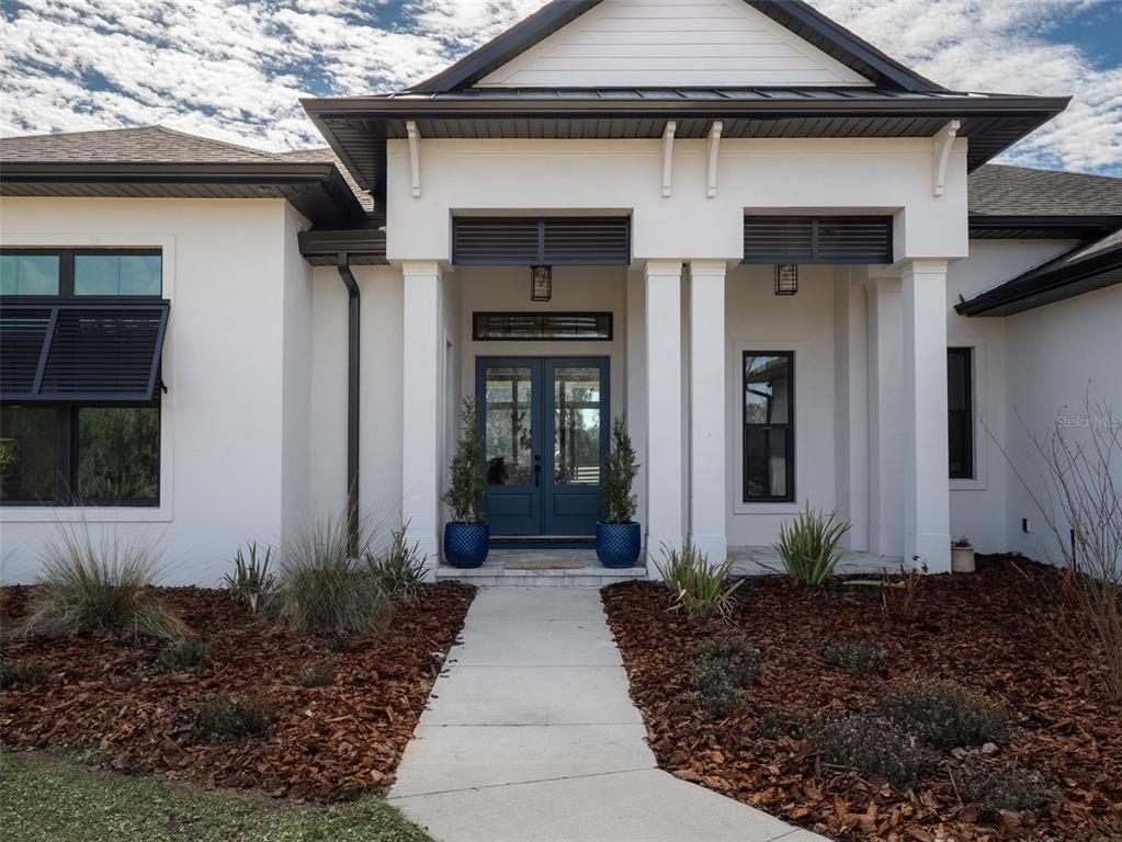 The exterior of a white house features a covered entryway with dark blue double doors — 11920 SE 22ND AVENUE ROAD, OCALA, FL