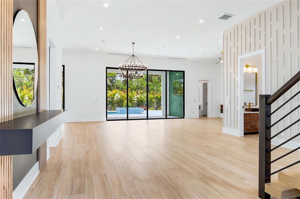 A spacious living area with light wood floors, a modern chandelier, and large sliding glass doors — 1870 JASMINE DRIVE, SARASOTA, FL