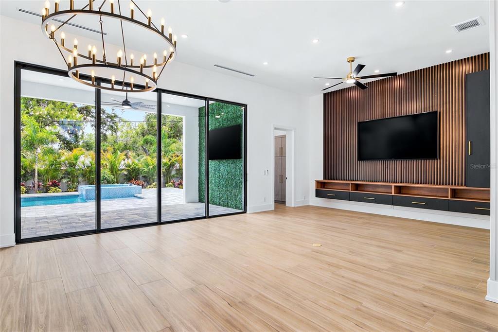 A modern living room features wood-slat wall paneling, a floating media console, and sliding glass doors — 1870 JASMINE DRIVE, SARASOTA, FL