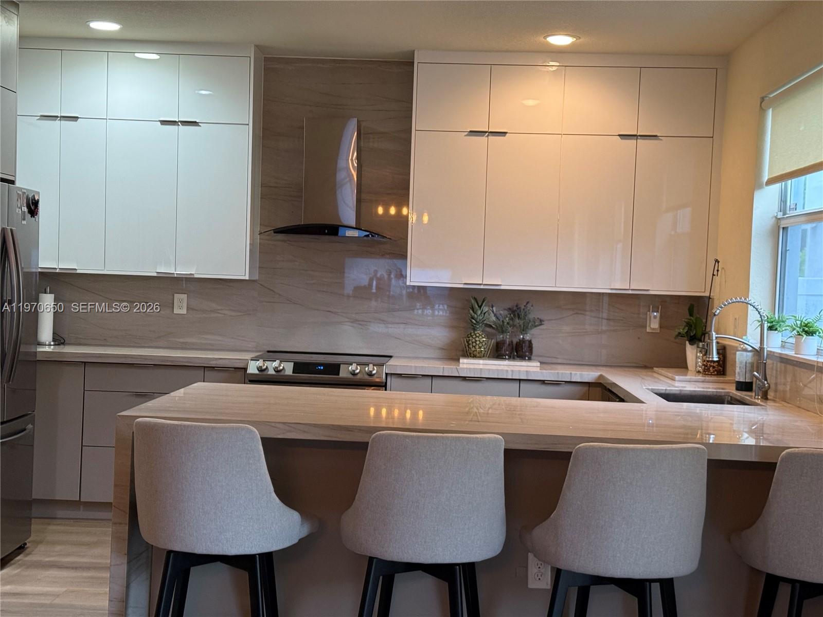 A modern kitchen features white glossy cabinets, a stone backsplash, and a breakfast bar with stools — 17012 SW 91st Ter, Miami FL 33196, MIAMI, FL