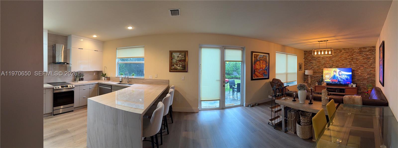 An open-concept kitchen and living area features light wood flooring, stone accent walls, and cabinetry — 17012 SW 91st Ter, Miami FL 33196, MIAMI, FL