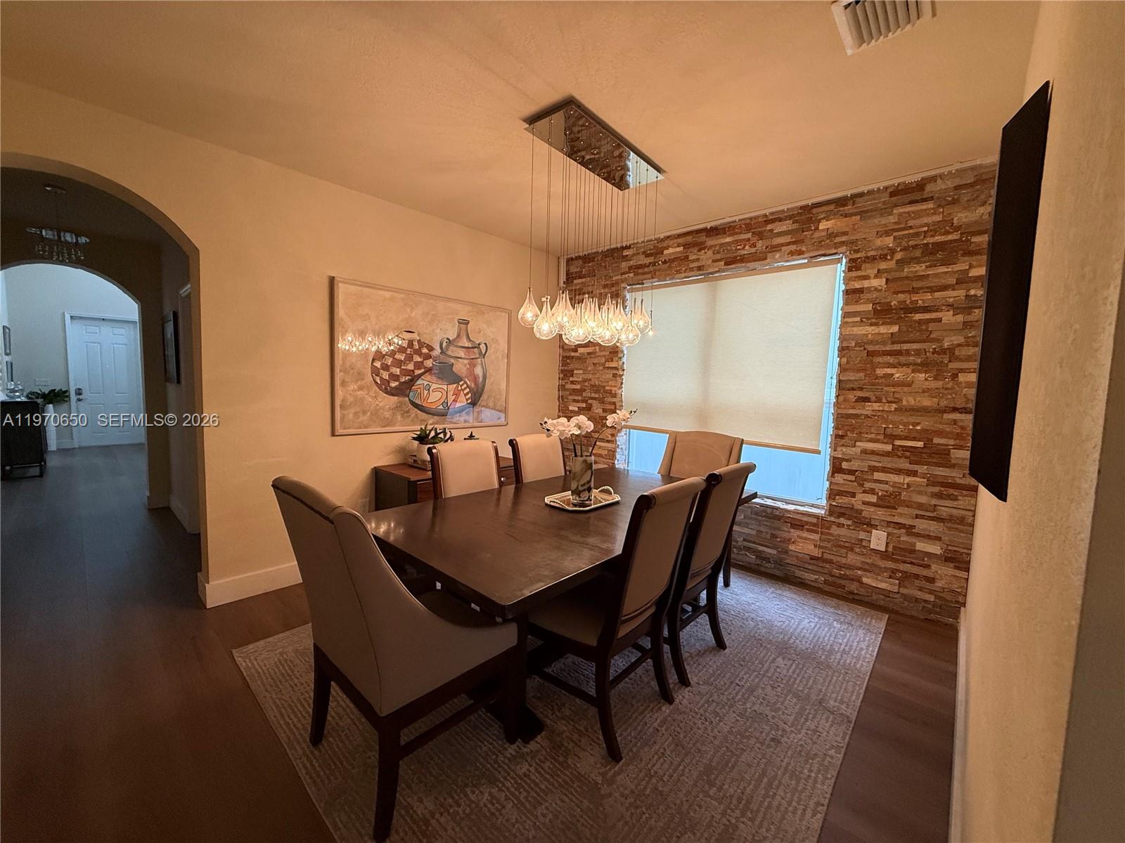 A dining room features a dark wood table, upholstered chairs, and a stone accent wall — 17012 SW 91st Ter, Miami FL 33196, MIAMI, FL