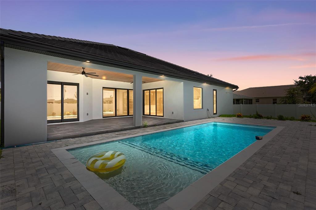 A modern house exterior features a covered patio, a swimming pool, and paver decking — 10 SW 33RD AVENUE, CAPE CORAL, FL