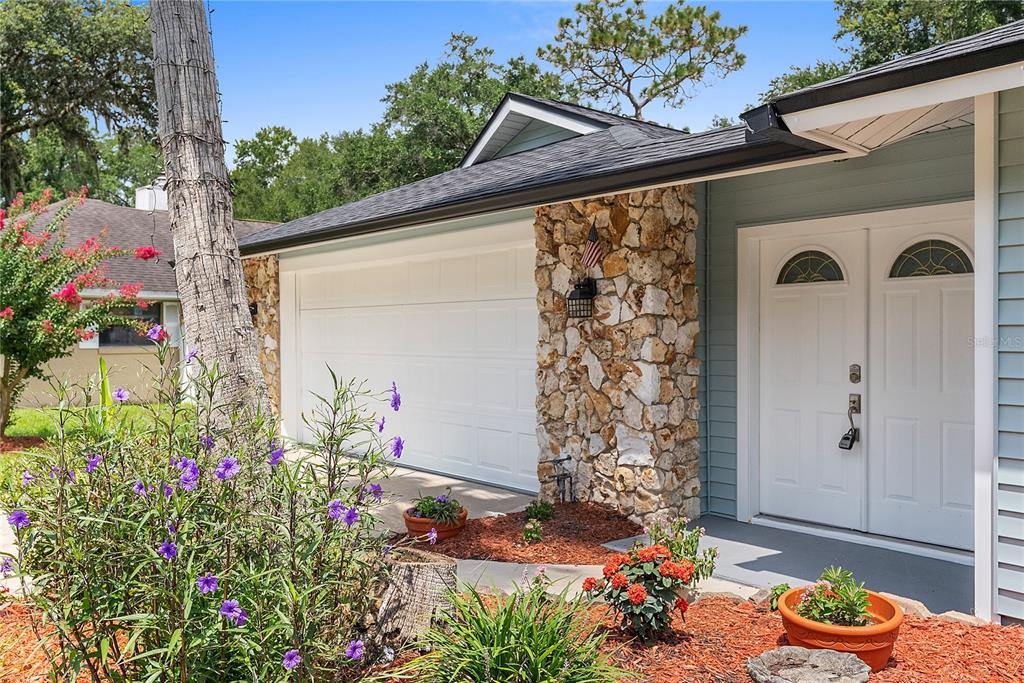 A house exterior features a stone pillar, a white garage door, and a double front door — 165 DUNCAN TRAIL, LONGWOOD, FL
