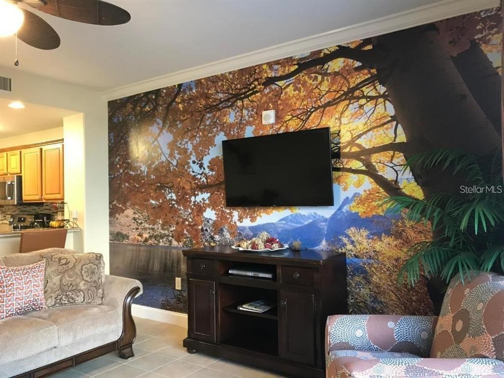 A living room features a large nature-themed wall mural, a television, and a wooden media console — 13415 BLUE HERON BEACH DRIVE UNIT 304, ORLANDO, FL