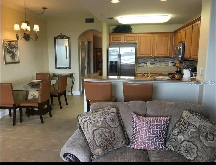 An open-concept kitchen with wood cabinets overlooks a dining area and a living room sofa — 13415 BLUE HERON BEACH DRIVE UNIT 304, ORLANDO, FL