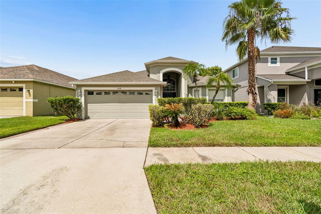 A single-story suburban house with a tan stucco exterior, a two-car garage, and palm trees — 19308 SANDY SPRINGS CIRCLE, LUTZ, FL