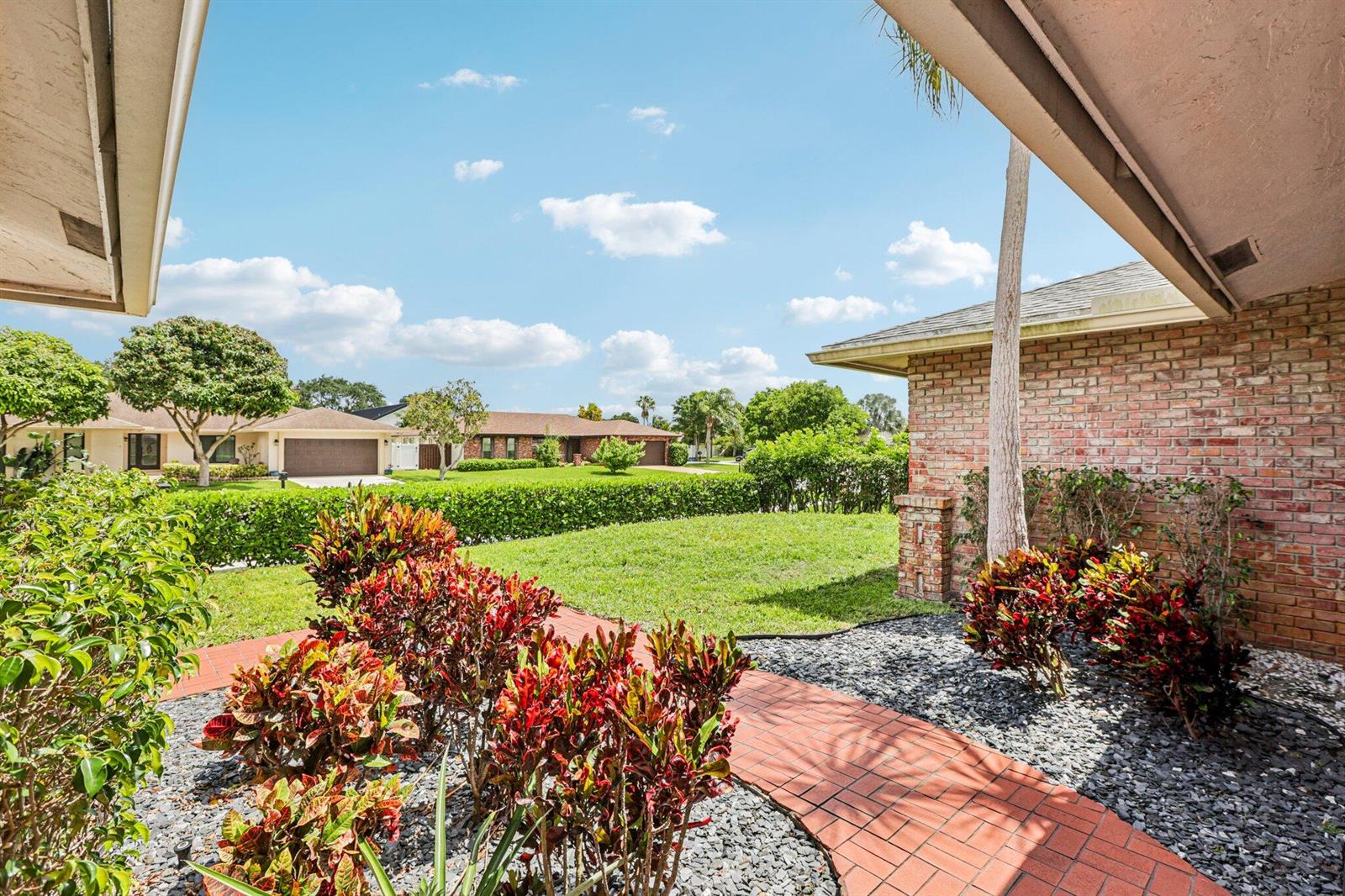 A brick walkway leads through a landscaped front yard toward a brick house exterior — 17679 Woodview Terrace, Boca Raton FL 33487, BOCA RATON, FL